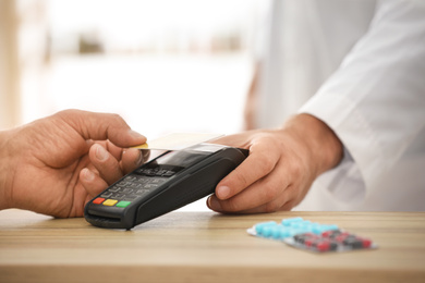 Customer using terminal for contactless payment with credit card in pharmacy, closeup