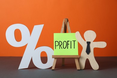Economic profit. Wooden figure, easel with note and percent sign on grey table against orange background