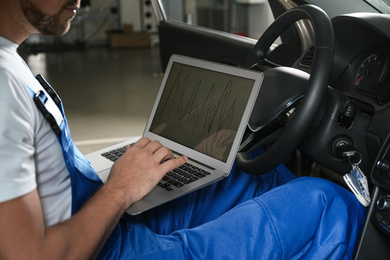 Mechanic with laptop doing car diagnostic at automobile repair shop, closeup