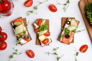 Tasty rye crispbreads with salmon, cream cheese and vegetables on light grey table, flat lay