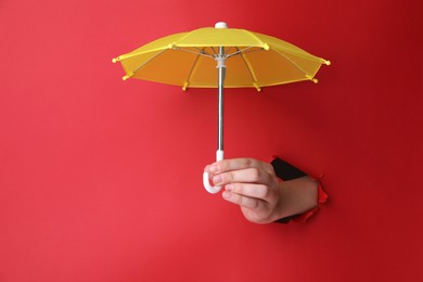 Woman holding open small yellow umbrella through hole in red paper, closeup