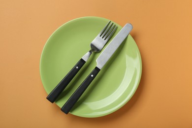 Photo of Green ceramic plate with cutlery on pale orange background, top view