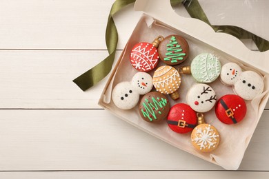 Photo of Beautifully decorated Christmas macarons in box and ribbon on white wooden table, flat lay. Space for text