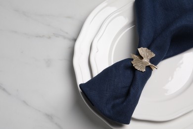 Plate with dark blue fabric napkin and decorative ring on white marble table, top view. Space for text
