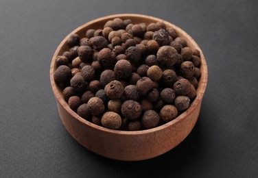 Photo of Wooden bowl of allspice grains on dark background
