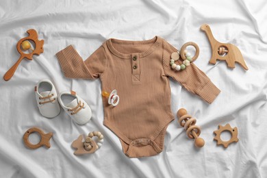 Flat lay composition with cute baby clothes and accessories on white bedsheet