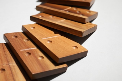 Fallen wooden domino tiles on light grey background, closeup