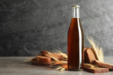 Photo of Bottle of delicious fresh kvass, spikelets and bread on grey table. Space for text