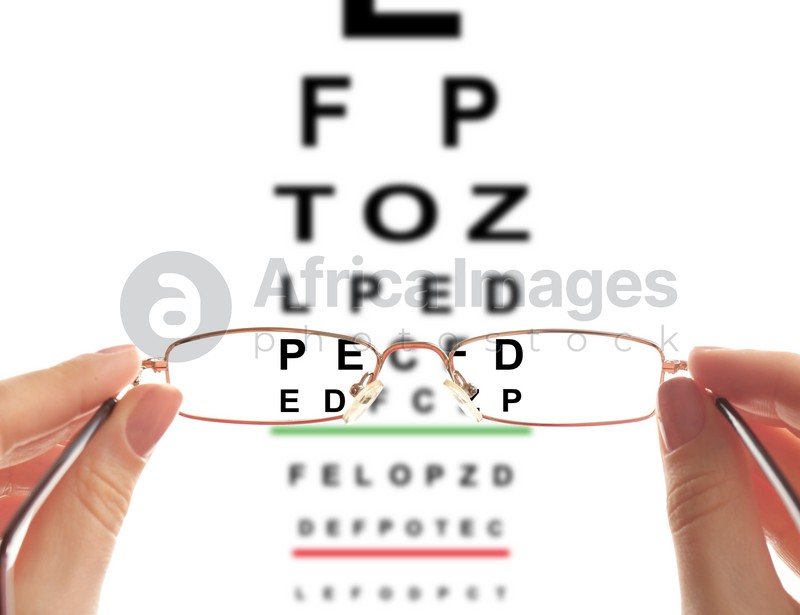 Woman holding glasses, closeup. View through lenses on eye chart, white background