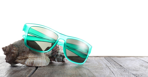Stylish sunglasses and shells on wooden table against white background. Space for text