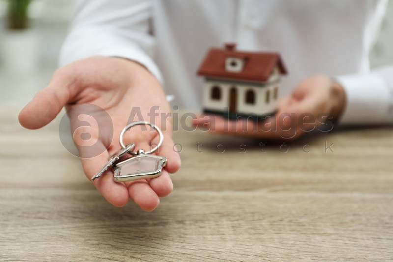 Real estate agent holding house key with trinket at wooden table, closeup