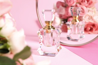 Bottle of perfume near mirror on pink background