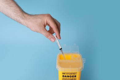 Man throwing used syringe into sharps container on light blue background, closeup