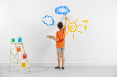 Little child painting cloud on white wall in room