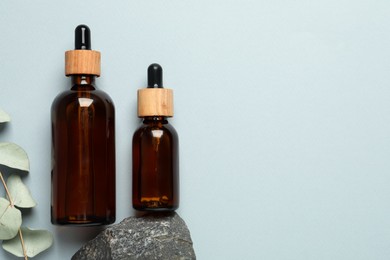 Flat lay composition with bottles of face serum, stone and eucalyptus branch on light grey background. Space for text