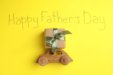Wooden car, gift box and phrase HAPPY FATHER'S DAY written on yellow background, flat lay