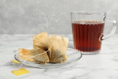 Saucer with used tea bags and cup of hot drink on white marble table