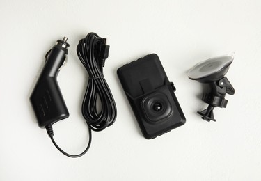 Modern car dashboard camera, suction mount and charger on white background, flat lay