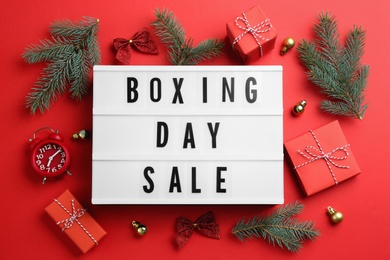 Lightbox with phrase BOXING DAY SALE and Christmas decorations on red background, flat lay