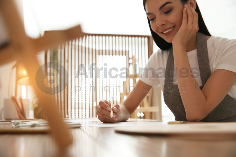 Young woman drawing with pencil at table indoors