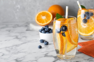 Photo of Delicious orange lemonade with soda water, mint and blueberries on white marble table, space for text. Fresh summer cocktail