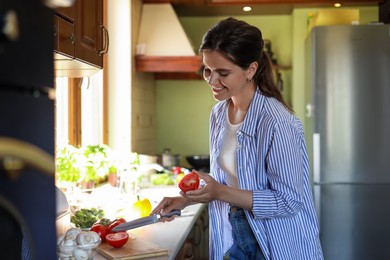 Young woman cutting fresh tomatoes at countertop in kitchen