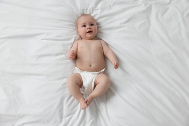 Photo of Cute little baby in diaper lying on white bed, top view