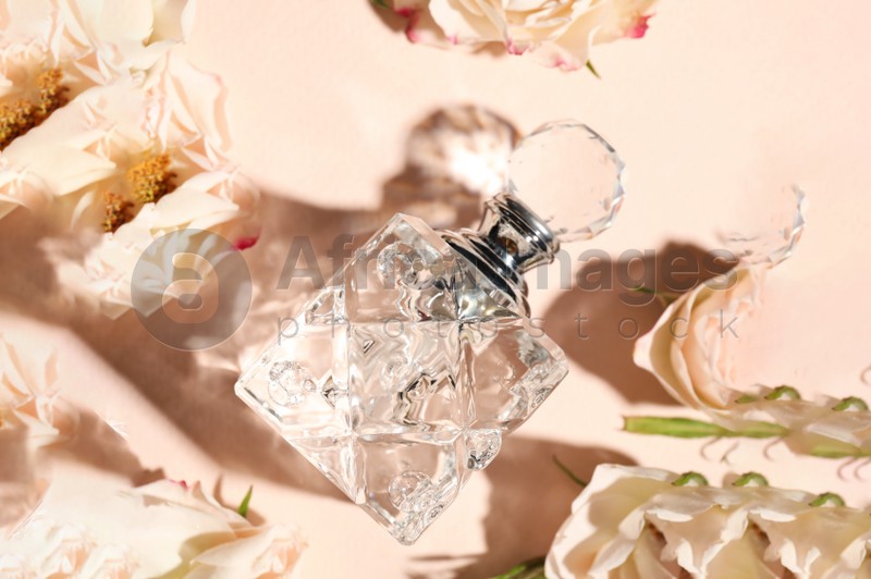 Bottle of aromatic perfume and flowers on beige background, flat lay