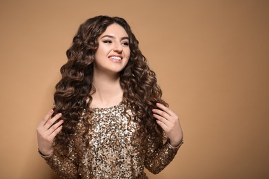 Photo of Beautiful young woman with long curly brown hair in golden sequin dress on beige background