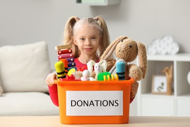 Cute little girl holding donation box with toys at home