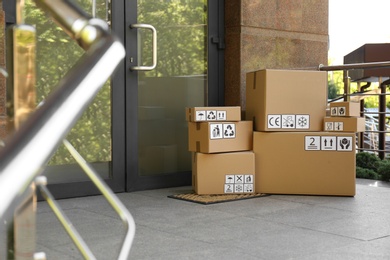 Cardboard boxes with different packaging symbols on door mat near entrance. Parcel delivery