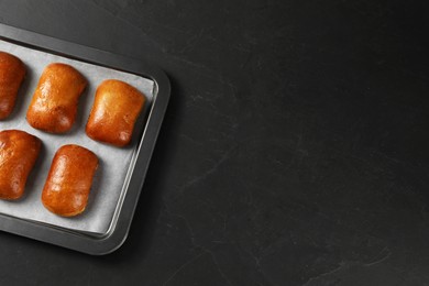 Photo of Delicious baked pirozhki on black table, top view. Space for text