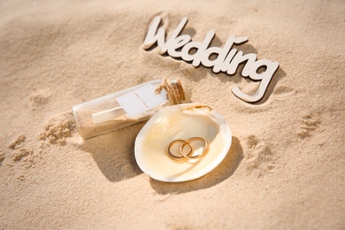 Shell with gold rings, invitation in glass bottle and word Wedding on sandy beach