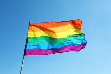 Rainbow LGBT flag fluttering on blue sky background. Gay rights movement