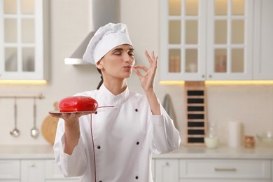 Professional confectioner with cake showing delicious gesture in kitchen