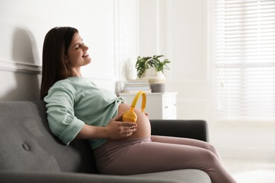 Beautiful pregnant woman with headphones on her belly at home