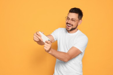 Emotional man playing game on smartphone against orange background