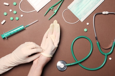 Doctor in sterile gloves with medical items on color background, top view