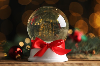 Beautiful snow globe on wooden table against blurred Christmas lights, closeup