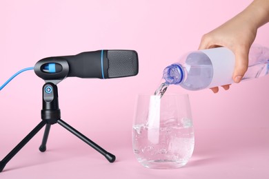 Woman making ASMR sounds with microphone and water on pink background, closeup