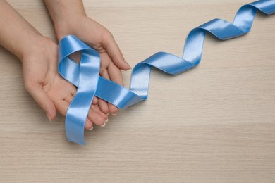 Photo of Woman holding light blue awareness ribbon at wooden table, top view. Space for text