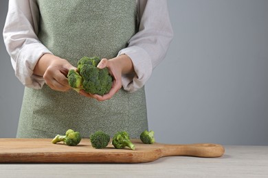 Woman separating fresh broccoli at wooden table, closeup. Space for text