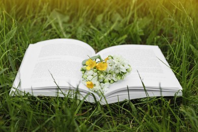 Open book with flowers on green grass outdoors