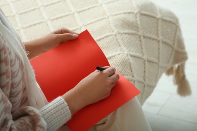 Young woman writing message in greeting card on bed, closeup. Space for text