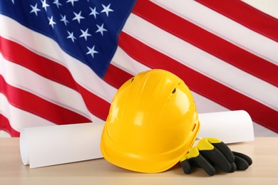Yellow hard hat, gloves and paper on light wooden table against American flag