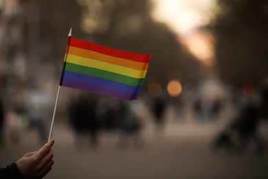 Woman holding small LGBT flag on city street, closeup. Space for text
