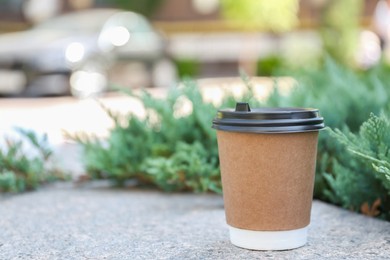 Disposable paper cup with plastic lid on stone parapet outdoors, space for text