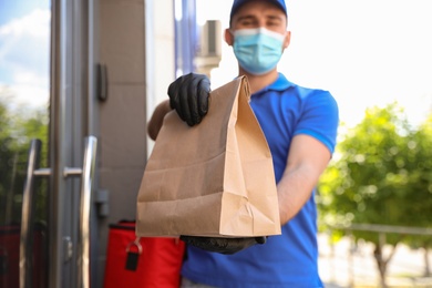 Courier in protective mask and gloves with order near front door, focus on hands. Restaurant delivery service during coronavirus quarantine