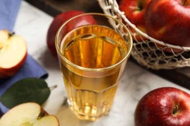 Glass of delicious cider and ripe red apples on white marble table, closeup