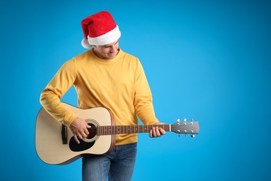 Man in Santa hat playing acoustic guitar on light blue background, space for text. Christmas music
